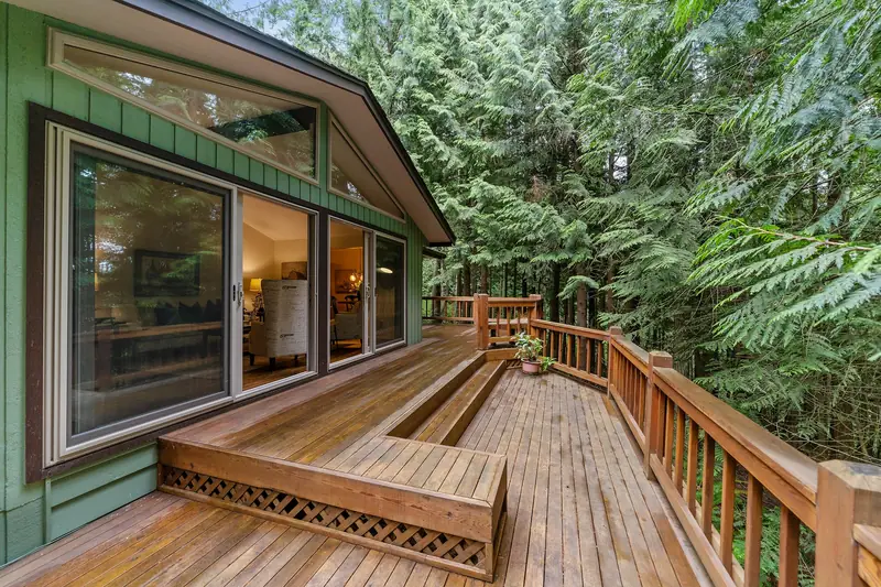 Wooden deck with railing and built-in steps beside a house in the woods